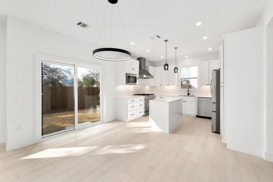 Kitchen with a kitchen island, white cabinets, stainless steel appliances, pendant lighting, and light wood finished floors