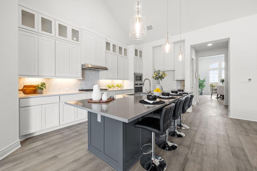 Kitchen with decorative backsplash, vaulted ceiling, an island with sink, light wood-style flooring, and white cabinets