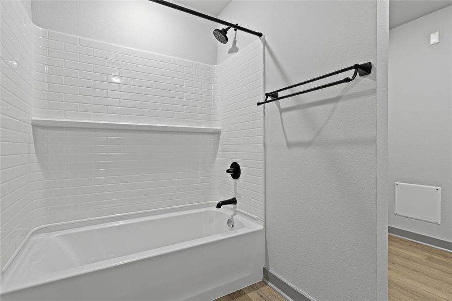 Bathroom featuring bathtub / shower combination, light wood-style floors, and a textured wall Bathroom featuring bathtub / shower combination, light wood-style floors, and a textured wall
