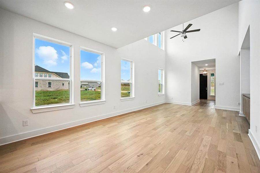 Unfurnished living room featuring plenty of natural light, light wood-style flooring, recessed lighting, a chandelier, and a high ceiling Unfurnished living room featuring plenty of natural light, light wood-style flooring, recessed lighting, a chandelier, and a high ceiling