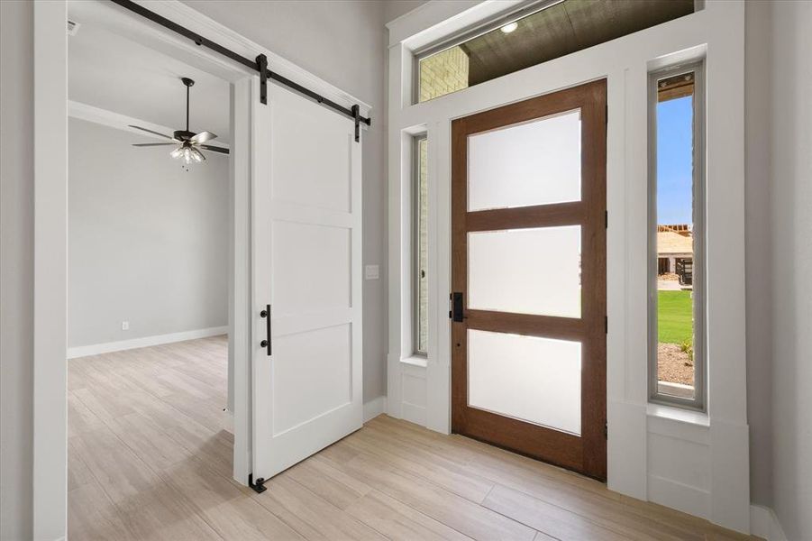 Modern wood-finish front door with frosted glass panels, flanked by sidelight windows and a transom window