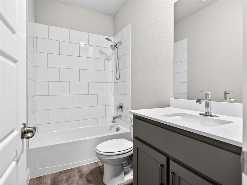 Bathroom featuring a white subway tile shower surround, a white bathtub, and a dark gray vanity with a white countertop and integrated sink Bathroom featuring a white subway tile shower surround, a white bathtub, and a dark gray vanity with a white countertop and integrated sink