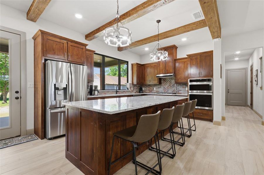 Contemporary kitchen featuring a spacious island with a light-toned countertop, rich wood cabinetry, stainless steel appliances, and wood-finish flooring