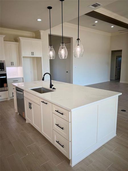 Kitchen featuring a center island with sink, white cabinets, ornamental molding, wood tiled floors, and stainless steel appliances Kitchen featuring a center island with sink, white cabinets, ornamental molding, wood tiled floors, and stainless steel appliances