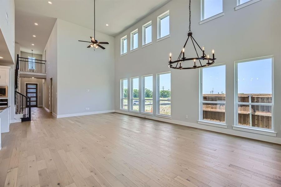 Unfurnished living room featuring a towering ceiling, a chandelier, light wood finished floors, baseboards, and recessed lighting Unfurnished living room featuring a towering ceiling, a chandelier, light wood finished floors, baseboards, and recessed lighting