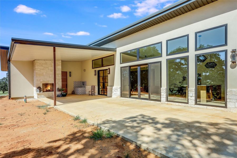 Rear view of property featuring stone siding, stucco siding, a patio area, and an outdoor stone fireplace