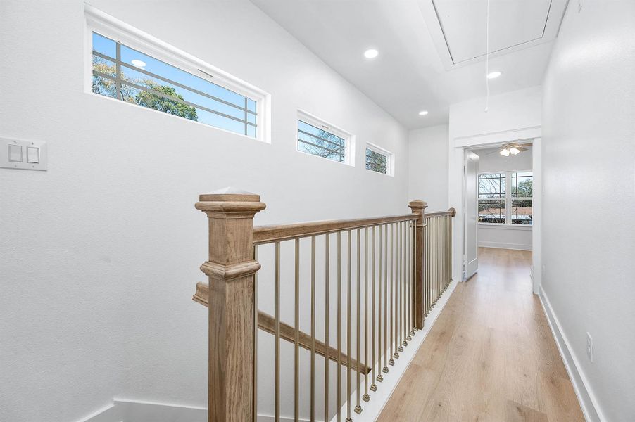 Upstairs hallway featuring natural light, wood railing details, and a bright open feel.