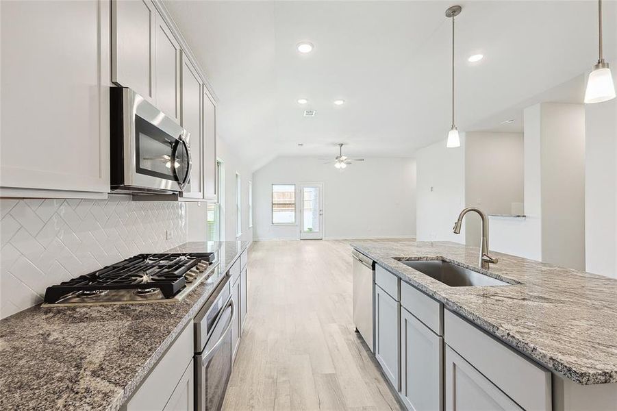 Kitchen with decorative light fixtures, sink, light hardwood / wood-style floors, appliances with stainless steel finishes, and backsplash