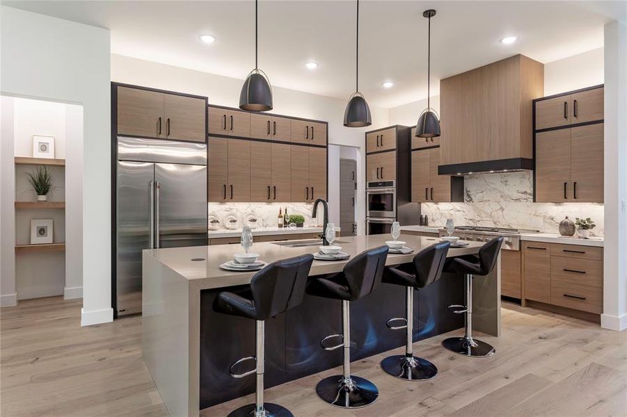 Kitchen with a breakfast bar, sink, appliances with stainless steel finishes, decorative light fixtures, and light hardwood / wood-style floors