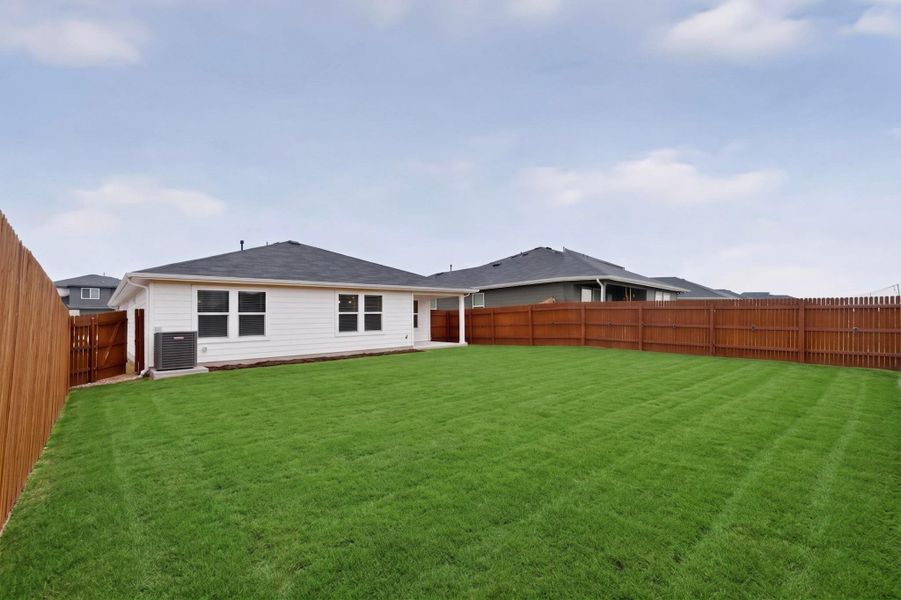 A spacious grassy lawn sits enclosed within privacy fencing behind this modern single-story residence.