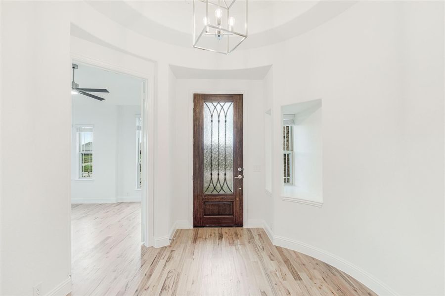 Bright home entryway with dark wood front door, glass panel, chandelier, and light hardwood floors