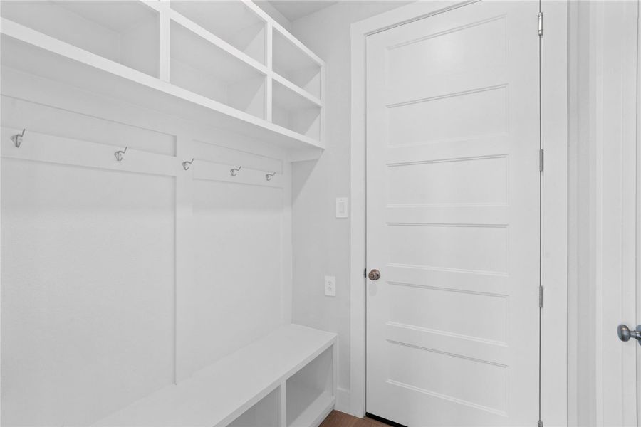 Step into this highly functional and stylish mudroom drop zone, an essential feature for a busy household. The space boasts custom-built white cabinetry and shelving, providing generous storage for coats, bags, and shoes. A comfortable built-in bench offers a convenient spot to sit, while three sleek hooks keep outerwear tidy and accessible.