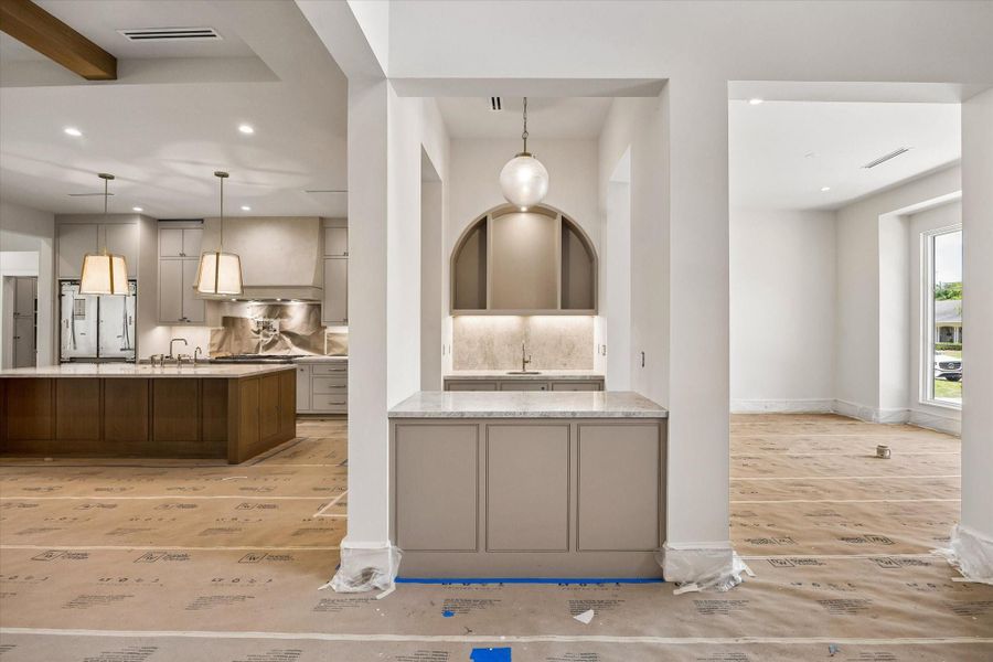 The wet bar and butler’s pantry is conveniently located between the family room, kitchen, and dining room. This thoughtfully designed space to include a built-in wine refrigerator, statement pendant lighting, a brass faucet with a copper sink, and elegant glass shelving.