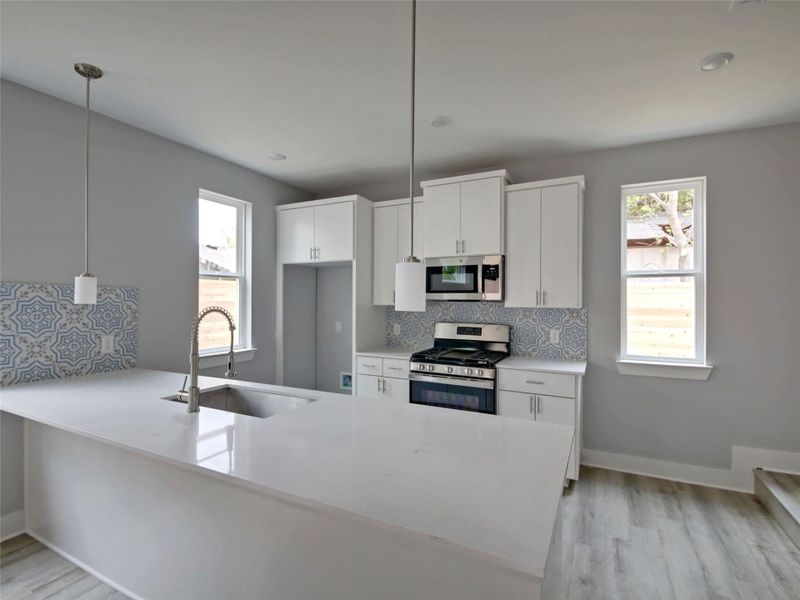 Kitchen with a peninsula, stainless steel appliances, pendant lighting, backsplash, and light wood-style flooring