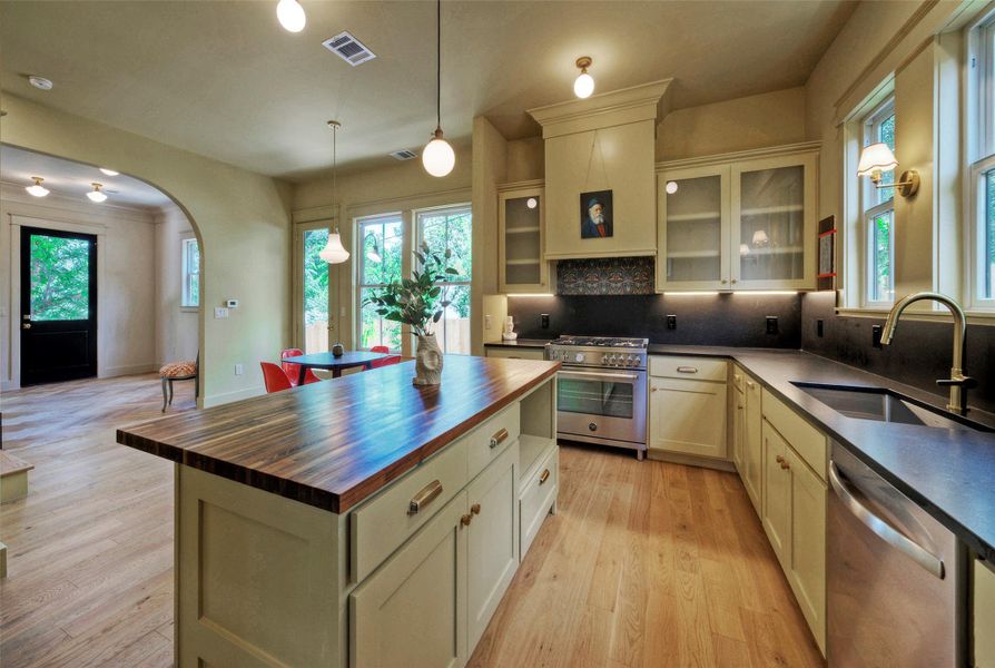 A grand central island with a wood countertop anchors this spacious kitchen, featuring modern appliances and ample natural light.