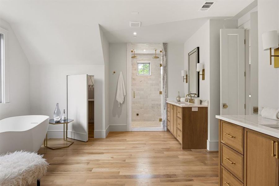 Freestanding tub with a window, glass-enclosed shower with a window, dual vanities with light wood-finish cabinetry, and light wood-finish flooring Freestanding tub with a window, glass-enclosed shower with a window, dual vanities with light wood-finish cabinetry, and light wood-finish flooring