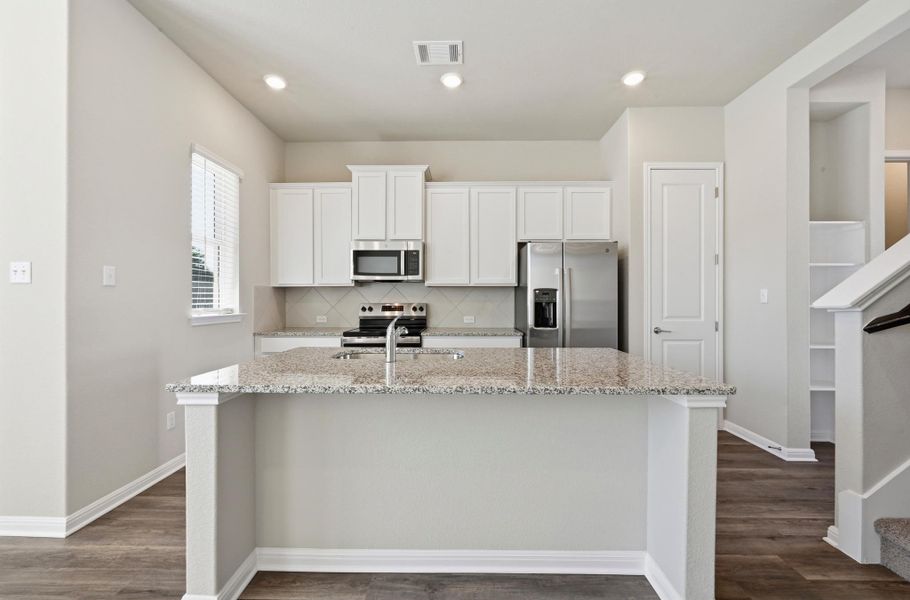 Kitchen featuring a central island with a light-toned granite countertop, white cabinetry, stainless steel appliances, a tile backsplash, and recessed lighting Kitchen featuring a central island with a light-toned granite countertop, white cabinetry, stainless steel appliances, a tile backsplash, and recessed lighting