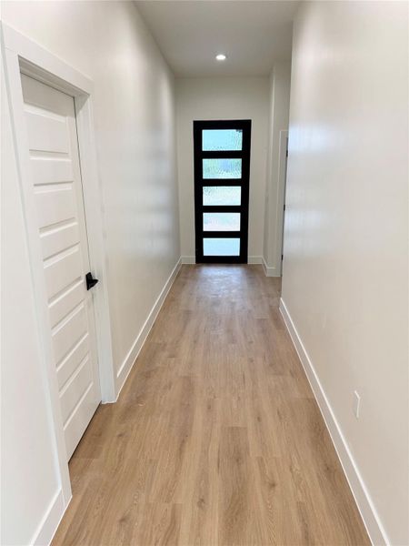 A well-lit hallway with natural wood-look flooring leads to an eye-catching contemporary entry door. A well-lit hallway with natural wood-look flooring leads to an eye-catching contemporary entry door.