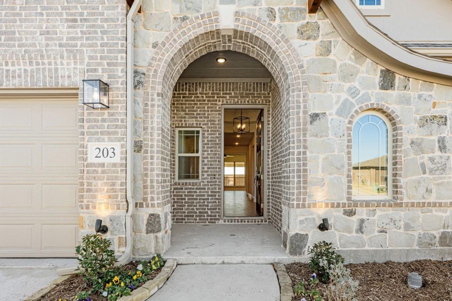 Home entrance with arched brick and stone surround, covered entryway, and garage door with house number 203.