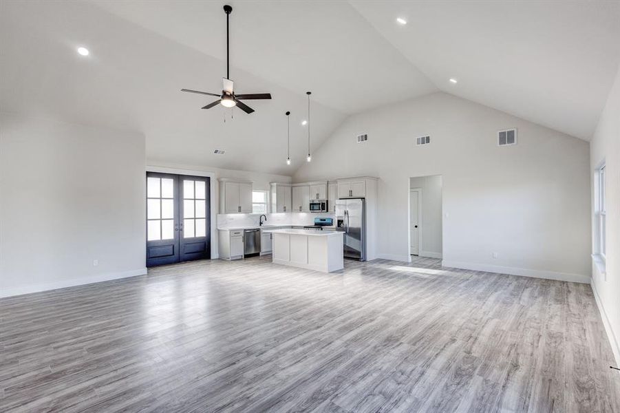 Unfurnished living room with ceiling fan, french doors, high vaulted ceiling, and light hardwood / wood-style flooring