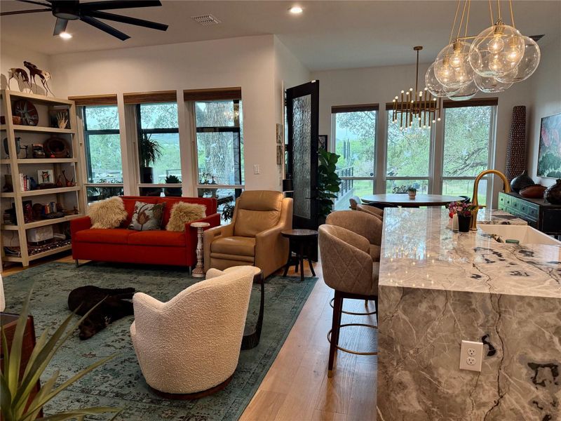 Open-concept living area featuring light wood-finish flooring, a contemporary ceiling fan, and large windows with natural light
