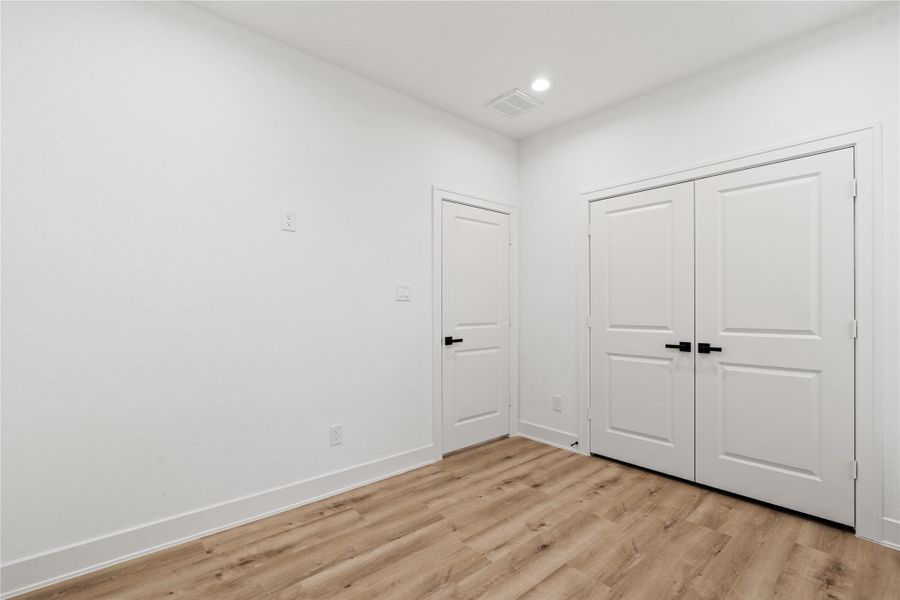 This thoughtfully designed bedroom balances simplicity and warmth with oak-colored floors, soft recessed lighting, and clean architectural lines. Dual closets offer functional storage while maintaining the home’s calm, modern aesthetic—a versatile space equally suited for guests or everyday living.
