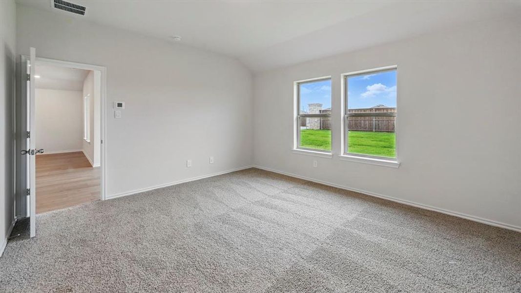 Empty room with vaulted ceiling and light colored carpet
