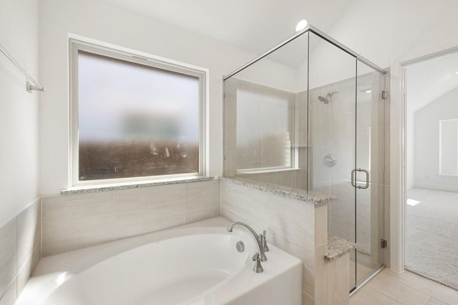 Master bathroom with soaking tub, glass-enclosed shower, and beige tile walls next to a frosted window