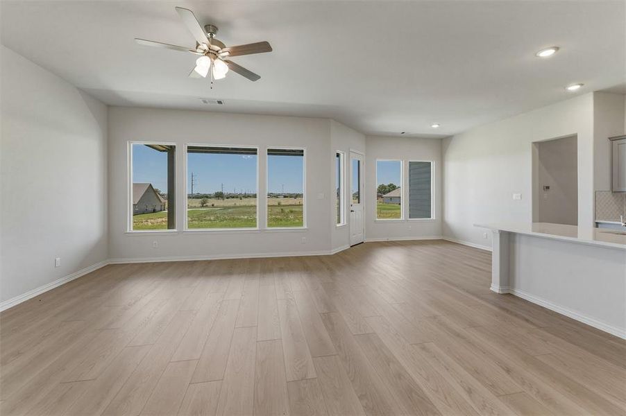 Spacious interior room featuring wood-finish flooring, a ceiling fan with integrated lighting, recessed lighting, and multiple windows