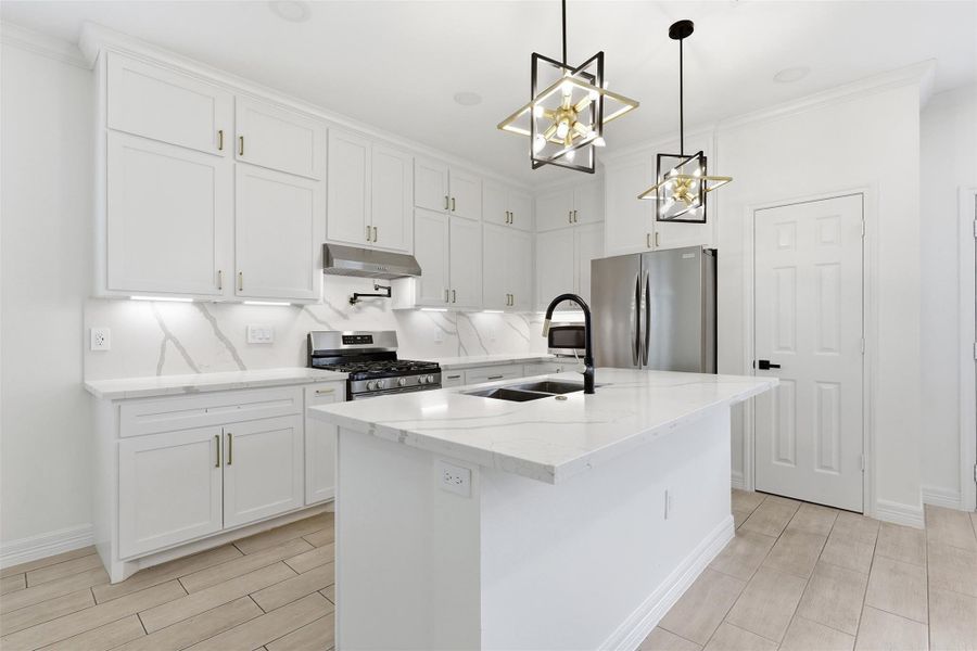 Kitchen island with white countertops, pendant lighting, tile backsplash, and stainless steel refrigerator.