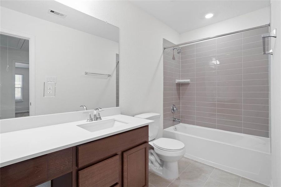 Secondary bath features tile flooring, bath/shower combo with tile surround, stained wood cabinets, beautiful light countertops, mirror, sleek fixtures and modern finishes.