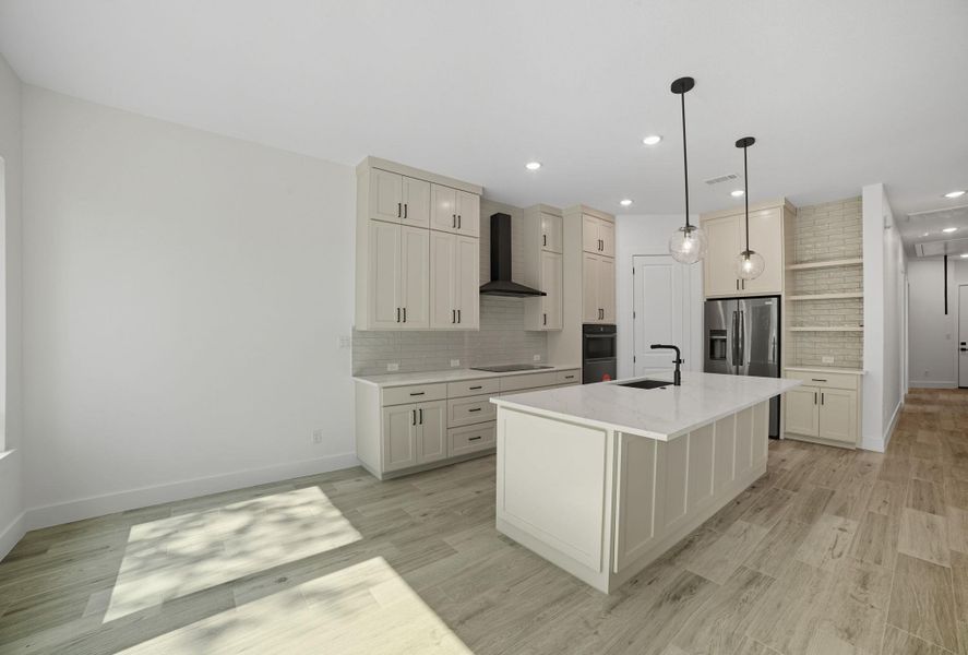 Kitchen with tasteful backsplash, pendant lighting, a center island with sink, open shelves, and wall chimney exhaust hood Kitchen with tasteful backsplash, pendant lighting, a center island with sink, open shelves, and wall chimney exhaust hood