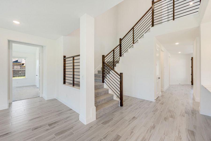 Open foyer with staircase featuring dark wood and metal railings, light wood-look tile floors, and white walls Open foyer with staircase featuring dark wood and metal railings, light wood-look tile floors, and white walls