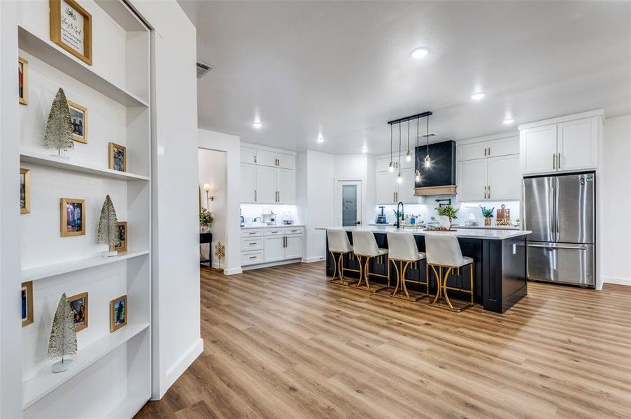 Kitchen with a kitchen breakfast bar, white cabinetry, decorative light fixtures, freestanding refrigerator, and a kitchen island with sink