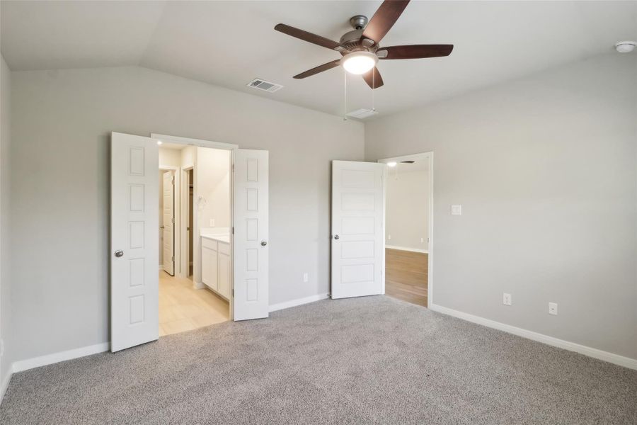 Unfurnished bedroom featuring light colored carpet, vaulted ceiling, baseboards, ensuite bathroom, and a ceiling fan Unfurnished bedroom featuring light colored carpet, vaulted ceiling, baseboards, ensuite bathroom, and a ceiling fan