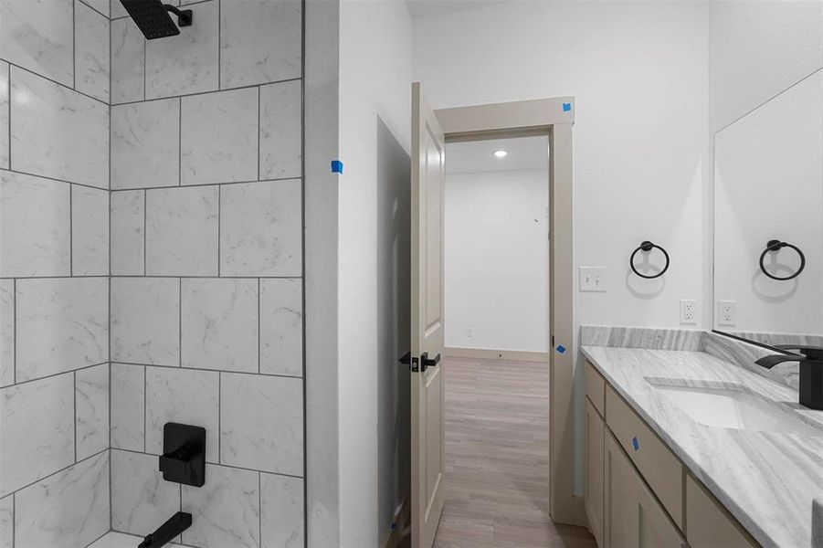 Bathroom with tiled shower, vanity, and wood finished floors
