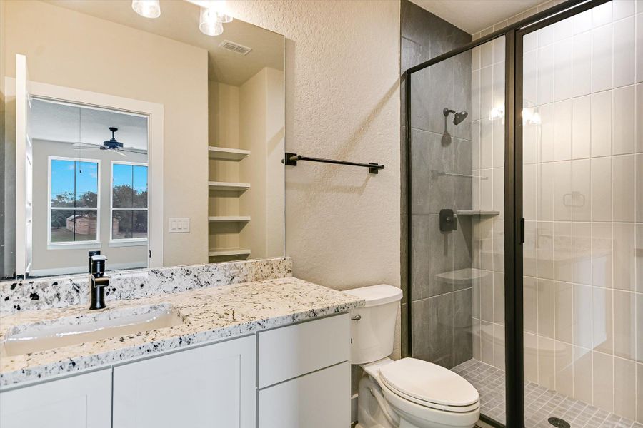 Full bath featuring a textured wall, a stall shower, vanity, and a ceiling fan