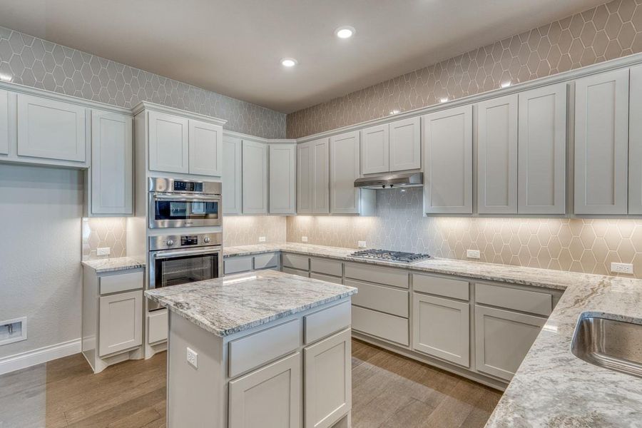Kitchen with decorative backsplash, light wood finished floors, recessed lighting, light stone countertops, and appliances with stainless steel finishes