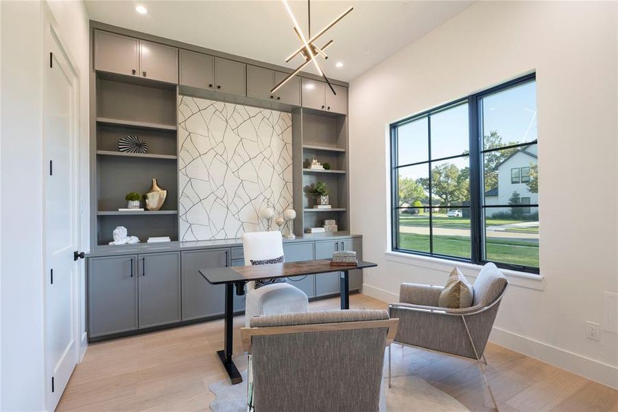 Home office with light hardwood / wood-style flooring and a notable chandelier