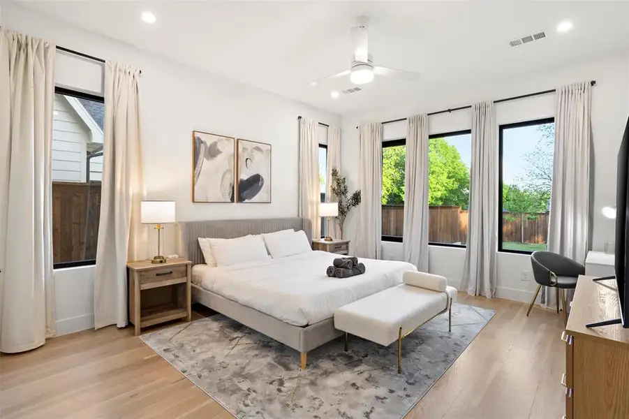 Spacious room featuring wood-finish flooring, a contemporary ceiling fan, recessed lighting, and multiple large windows with light-toned drapes