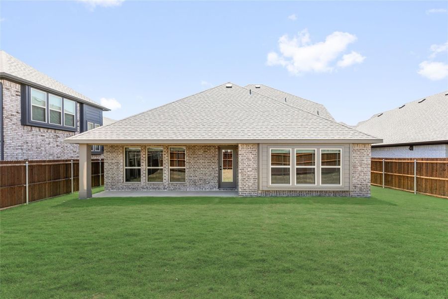 Rear exterior of brick home with covered patio, large fenced backyard, and green lawn Rear exterior of brick home with covered patio, large fenced backyard, and green lawn