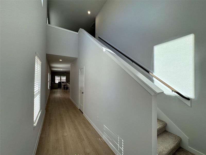 Bright, modern hallway with light wood flooring and a staircase leading to an upper level. The space is well-lit with natural light from windows, and the hallway leads towards the kitchen and an open living area. Bright, modern hallway with light wood flooring and a staircase leading to an upper level. The space is well-lit with natural light from windows, and the hallway leads towards the kitchen and an open living area.