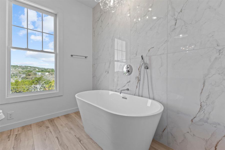 Bathroom featuring a freestanding bath, light wood-style flooring, stone wall, and tile walls