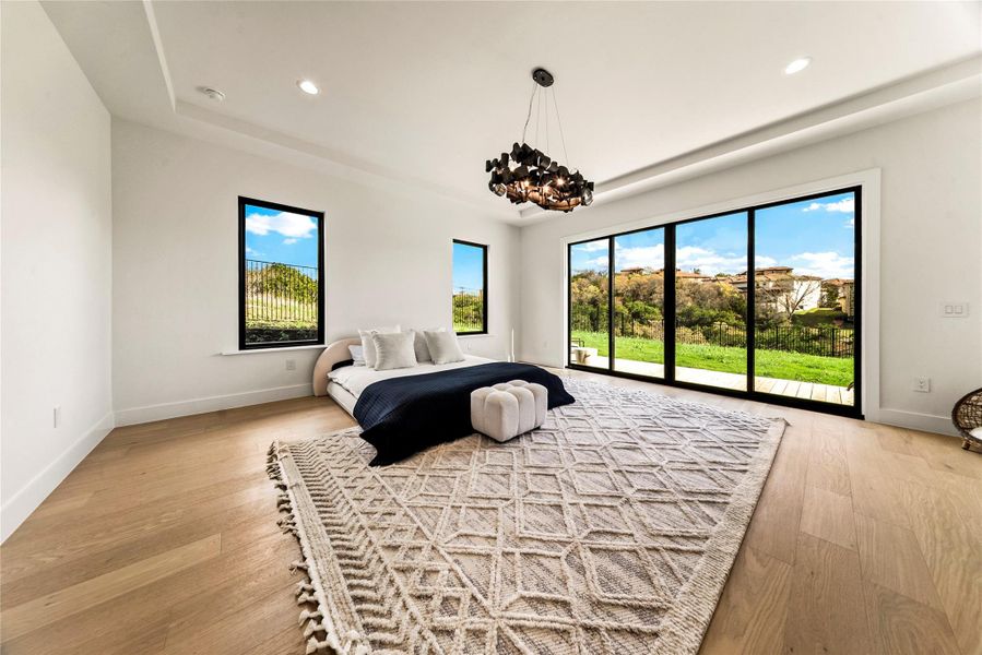 Bedroom with light wood-type flooring, access to outside, hanging lights, and a raised ceiling Bedroom with light wood-type flooring, access to outside, hanging lights, and a raised ceiling