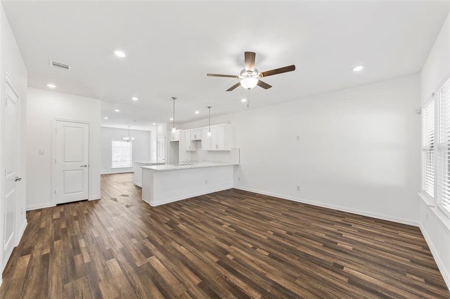 Unfurnished living room featuring ceiling fan with notable chandelier and dark hardwood / wood-style flooring