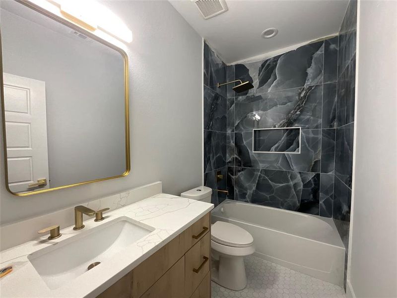 Bathroom featuring a wood-finish vanity with a quartz countertop, an undermount sink with brass fixtures, and a gold-framed mirror Bathroom featuring a wood-finish vanity with a quartz countertop, an undermount sink with brass fixtures, and a gold-framed mirror