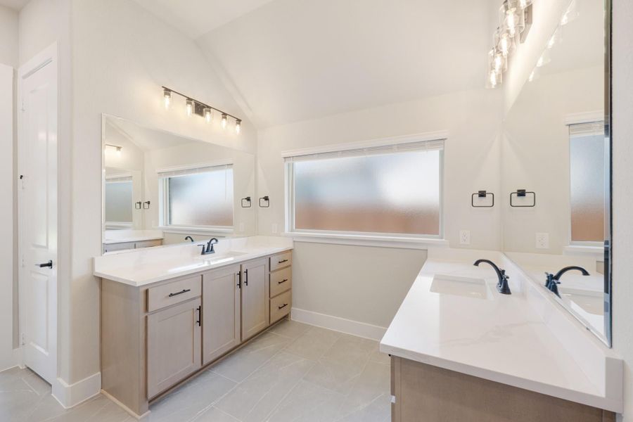 Bathroom with dual vanities, white quartz countertops, vaulted ceiling, and frosted windows