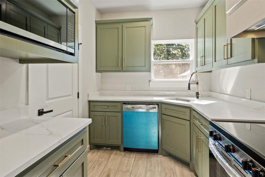 Kitchen featuring sage green cabinetry, white countertops, stainless steel appliances, and wood-finish tile flooring Kitchen featuring sage green cabinetry, white countertops, stainless steel appliances, and wood-finish tile flooring
