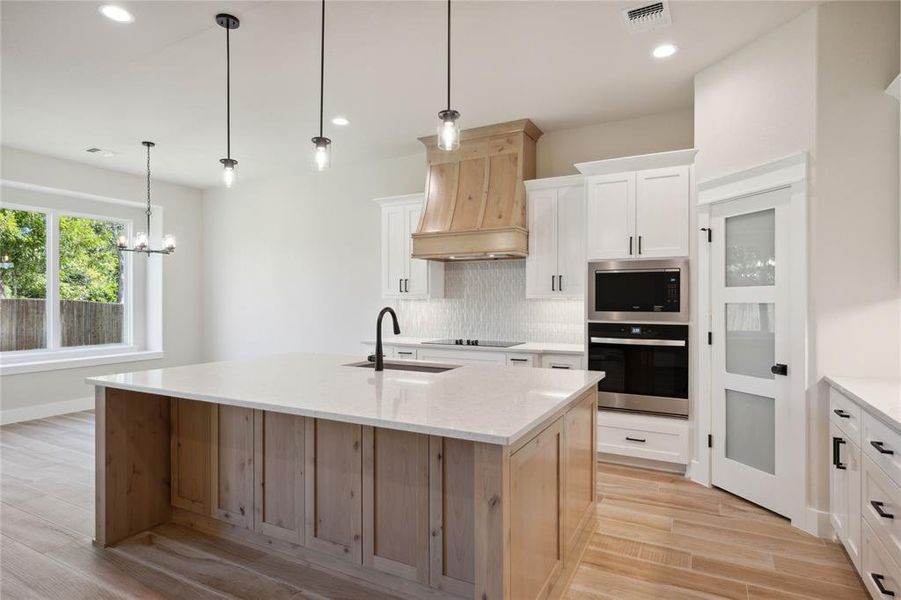 Kitchen with appliances with stainless steel finishes, custom range hood, sink, white cabinets, and an island with sink