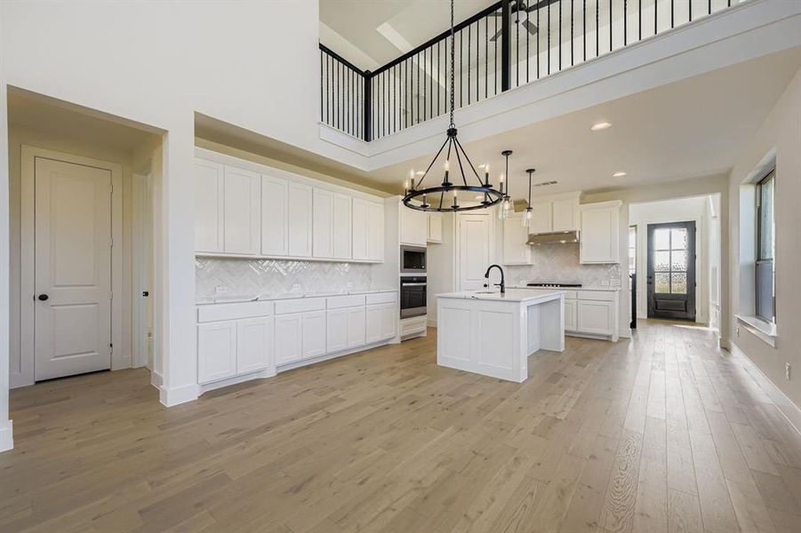Kitchen featuring white cabinets, a towering ceiling, decorative light fixtures, light wood-style flooring, and backsplash